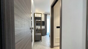 A modern hotel corridor with a wooden door, a bathroom with a mirror, and a seating area with a table and chairs. - Dolmen Guest House (Alghero)