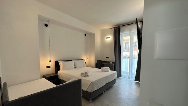 A hotel room with a bed, a desk, and a chair. There is a window with curtains. - Dolmen Guest House (Alghero)