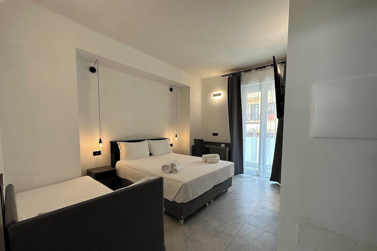 A hotel room with a bed, a desk, and a chair. There is a window with curtains.