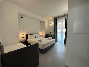 A hotel room with a bed, a desk, and a chair. There is a window with curtains. - Dolmen Guest House (Alghero)