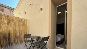 A small outdoor seating area with a table and chairs, a bamboo fence, and a view into a room with a bed and a window. - Dolmen Guest House (Alghero)