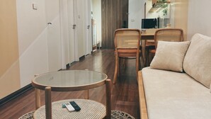 Ett hotellrum med trägolv, ett runt bord med en fjärrkontroll, en soffa och en matplats med stolar.