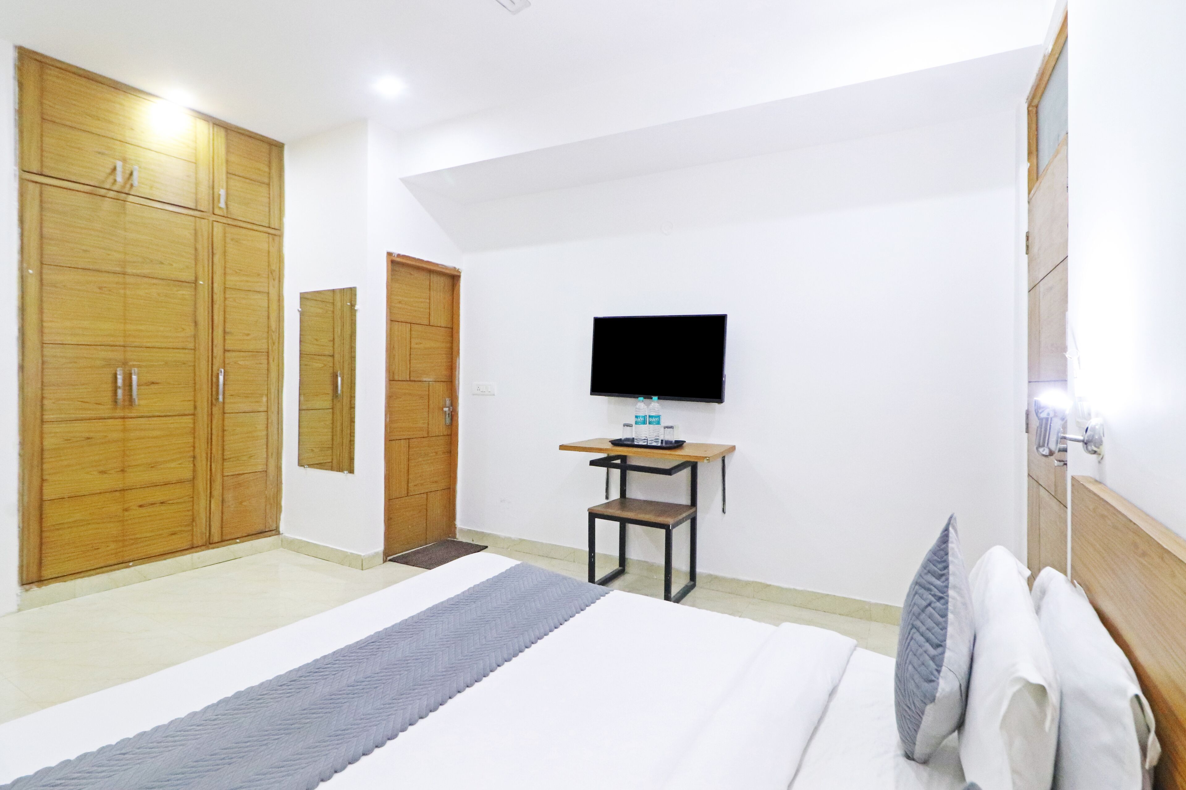 A bedroom with a bed, a TV, a wooden wardrobe, and a small table with a chair.