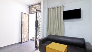 Ein Wohnzimmer mit schwarzem Ledersofa, einem Holztisch, einem flachbildfernseher an der Wand und einer teilweise geöffneten Tür mit dekorativem Gitter.
