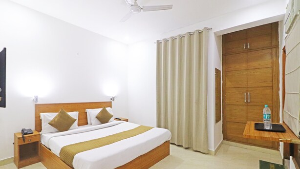 Ein Hotelzimmer mit einem Holzbett, einem Nachttisch, einem Deckenventilator, einem Kleiderschrank und einem kleinen Tisch mit einer Wasserflasche.
