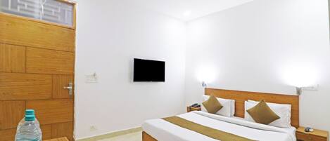 A hotel room with a wooden bed, a flat-screen TV, a bedside table, and a water bottle on a tray.