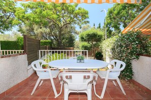 Une terrasse avec une table ronde et quatre chaises blanches, entourée d’une clôture blanche et de verdure.