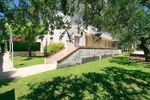 Un bâtiment doté d’un escalier en pierre menant à une porte, le tout étant entouré d’une pelouse bien entretenue et d’arbres.