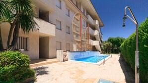 Area piscina con piscina cristallina azzurra, una palma e un edificio con balconi.