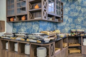 A buffet setup with multiple serving stations, wooden shelves, and a blue patterned wall. - Hotel Willa Tatrzańska (Krynica-Zdroj)