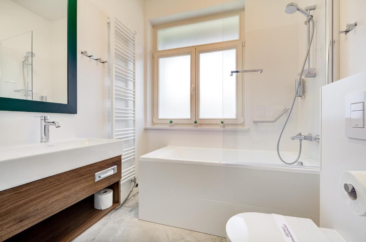 Un baño moderno con un espejo grande, un lavamanos blanco, una bañera y una ventana.