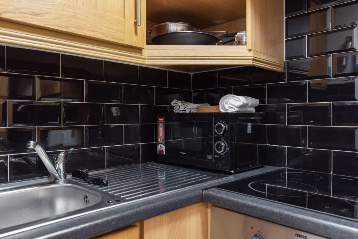 Una cocina con salpicadero de azulejos negros, un lavamanos de acero inoxidable y un horno empotrado.