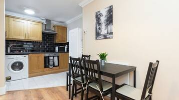 A compact kitchen with wooden cabinets, a washing machine, and a dining area with a table and chairs.