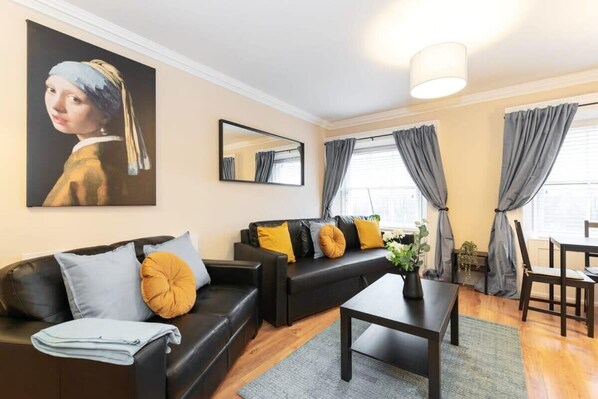 A modern living room with a black sofa, a coffee table, and a painting of a woman on the wall. - Central 1BED APT RELIABLE FAST WIFI & TV (Dublin 1)