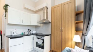 Una cocina compacta con gabinetes blancos, una encimera negra, una campana extractora de acero inoxidable y un horno integrado.