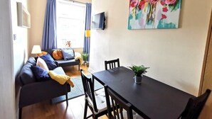 Un salon moderne avec une table à manger en bois foncé, un canapé agrémenté de coussins colorés et un tableau représentant des fleurs accroché au mur.