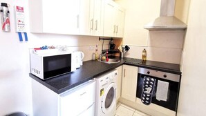 Une cuisine compacte avec des meubles blancs, un four à micro-ondes, un lave-linge et un four encastré.