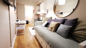 A compact living space with a sofa, a dining table, a small kitchen area, and a large mirror. - Cosy Studio right in city centre (Dublin 1)