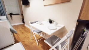 A compact kitchen with a white table, two chairs, a refrigerator, and a small potted plant. - Cosy Studio right in city centre (Dublin 1)