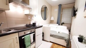 A compact hotel room with a kitchenette, a bed, a bedside table, a mirror, and a window with curtains. - Cosy Studio right in city centre (Dublin 1)