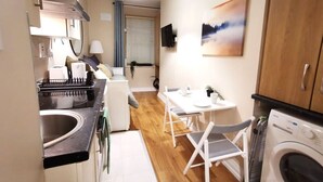 A compact kitchen with a sink, a washing machine, and a dining area with a table and chairs. - Cosy Studio right in city centre (Dublin 1)