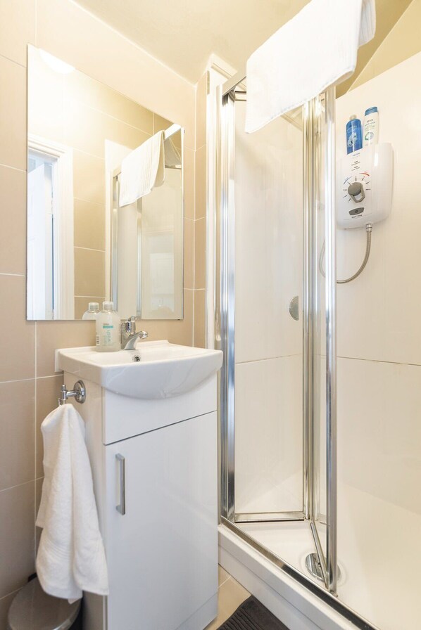 Ein Badezimmer mit einem weißen Waschbecken, einem Spiegel, einer Duschkabine aus Glas und einer Handbrause.