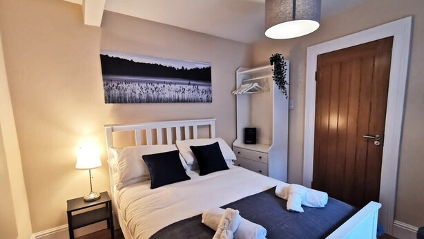 Un dormitorio ordenado con cama, mesitas de noche, lámpara, un cuadro y un armario.
