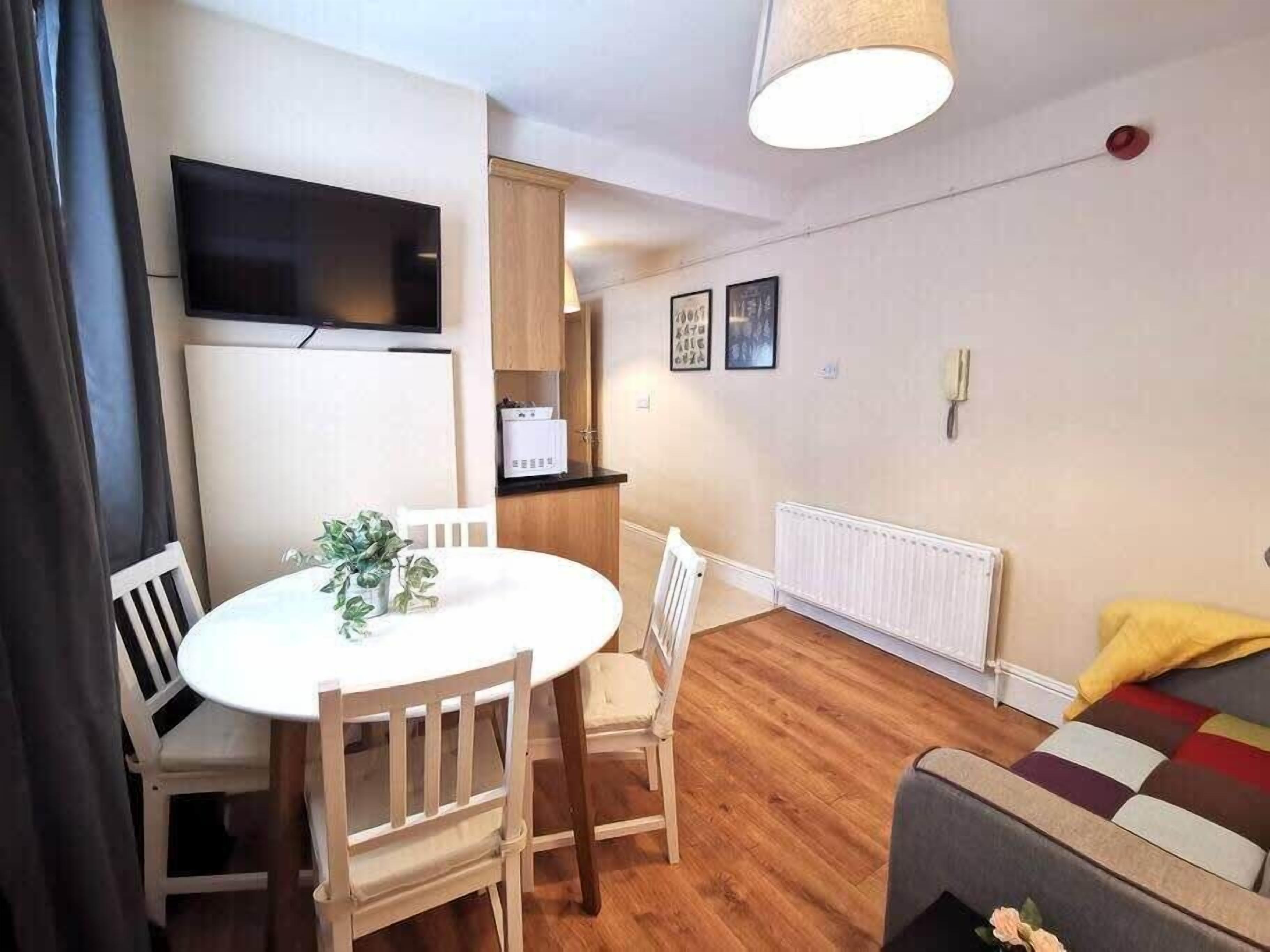 Un ambiente compatto con un tavolo da pranzo, sedie, un divano, una TV fissata al muro e un termosifone.