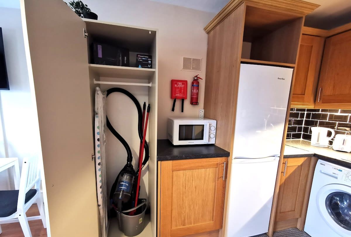 A compact kitchen with a microwave, a washing machine, and a fire extinguisher.