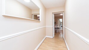 Un corridoio con pavimento in legno e pareti color crema, che conduce a una stanza con lavatrice e una sedia.