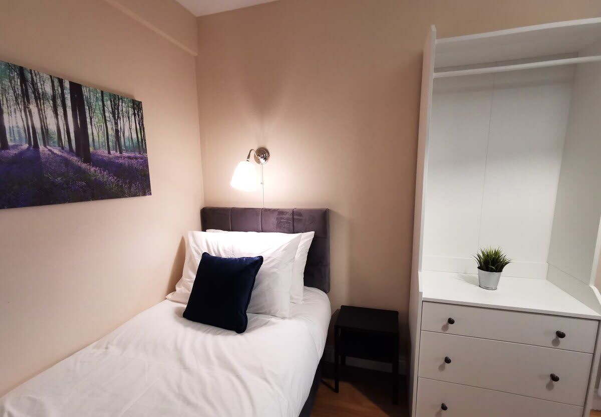 A bedroom with a bed, a bedside table, a lamp, a wardrobe, and a painting on the wall.