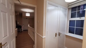 Un couloir doté d’un plancher en bois, de portes blanches et d’une fenêtre donnant sur l’extérieur.