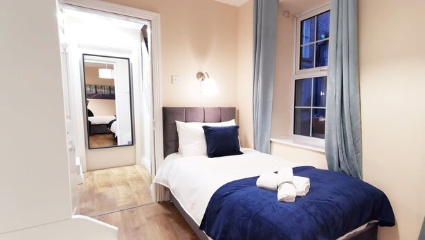 Une chambre à coucher avec un lit, une table de chevet, une fenêtre avec des rideaux et un miroir.