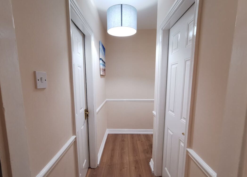 A hallway with white doors, a light fixture, and a framed picture on the wall.
