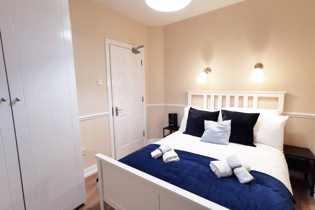 A bedroom with a white bed, dark blue bedspread, white headboard, and two bedside lamps.