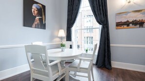 Un comedor con una mesa redonda y sillas blancas, una lámpara y dos cuadros en las paredes.