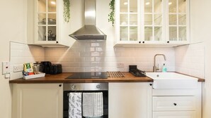 Una cocina con armarios blancos, una campana extractora de acero inoxidable, una encimera de madera, un horno empotrado y un lavamanos con grifo.