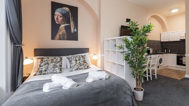 Une chambre d’hôtel moderne équipée d’un lit, d’une plante en pot, d’un tableau et d’une kitchenette.