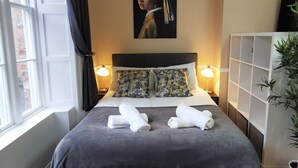 Une chambre d’hôtel avec un lit, deux lampes de chevet, un tableau au-dessus du lit et une fenêtre avec des rideaux.