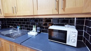 Una cucina con mobili in legno, uno schienale piastrellato nero, un forno a microonde e un lavandino con scolapiatti.