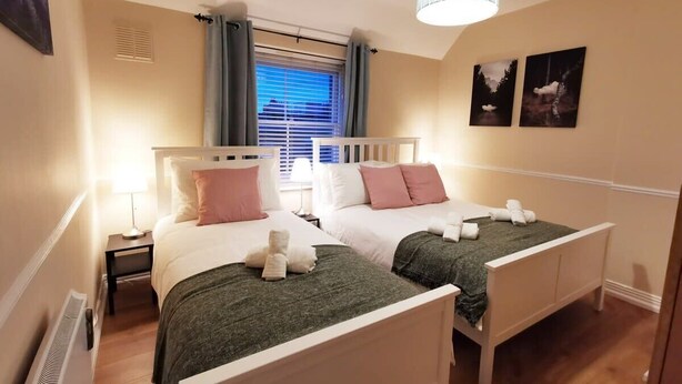 Una camera d'albergo con due letti singoli, una finestra con tende, una lampada a soffitto e due quadri appesi al muro.