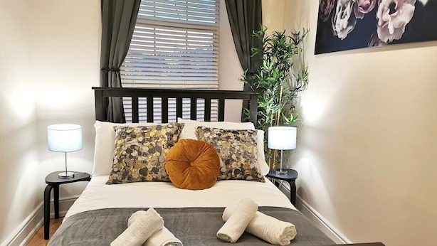 A neatly made bed with floral and solid pillows, two bedside lamps, and a pair of towels on the bed. - Central 1bed apartment with reliable fast WIFI (Dublin 1)