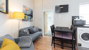 Un espace de vie compact comprenant un canapé, une table à manger avec des chaises, un téléviseur fixé au mur et un lave-linge.