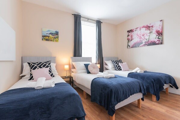 A hotel room with two beds, a window with curtains, and a painting on the wall.