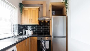 Une cuisine compacte avec des meubles en bois, un réfrigérateur en acier inoxydable, un crédence en carreaux noirs et un four encastré.