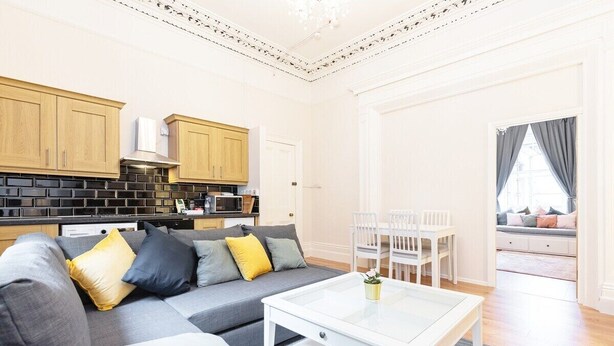 Een moderne woonkamer met een grijze bank, een witte salontafel en een eethoek met witte stoelen.