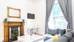 Een woonkamer met een open haard, een witte salontafel, een grijze bank en een aan de muur bevestigde televisie.