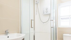 Een moderne badkamer met een glazen douchecabine, een witte wastafel en een toilet.