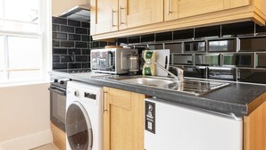Een keuken met houten kastjes, een wasmachine en een magnetron.