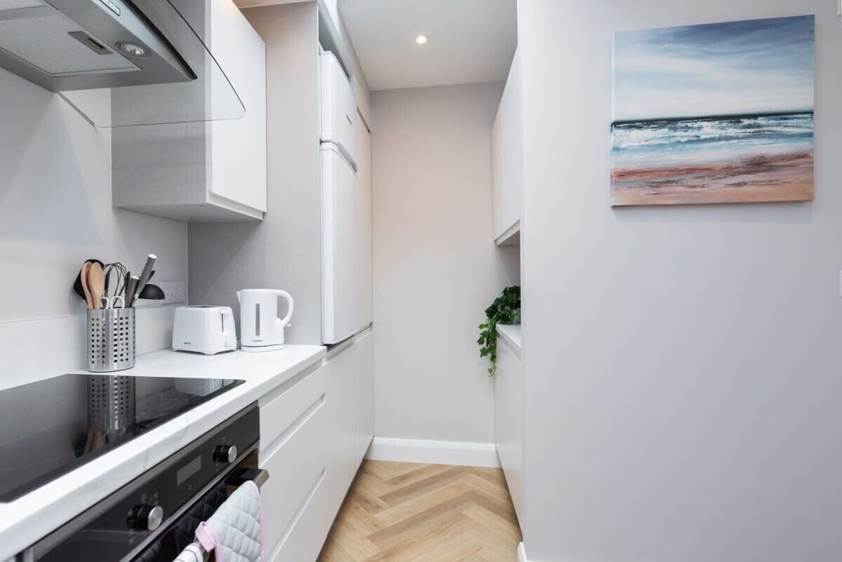 Une cuisine moderne avec des meubles blancs, une plaque de cuisson noire et un plancher en bois disposé en motif «arête de poisson» (ou «chevron»).